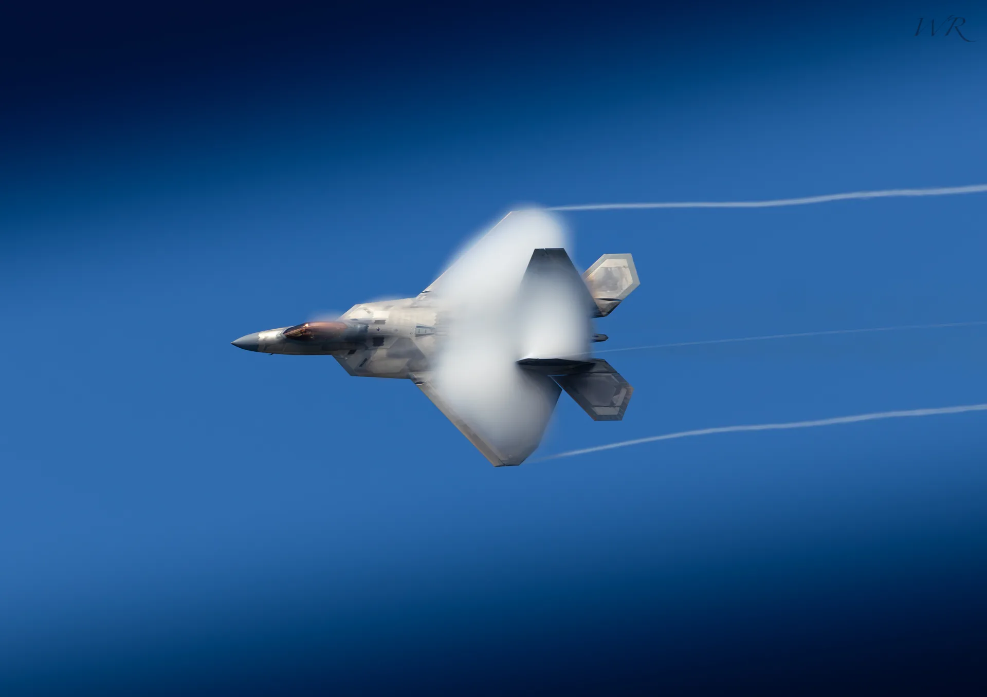 Fighter jet crossing a deep blue sky with a vapor trail