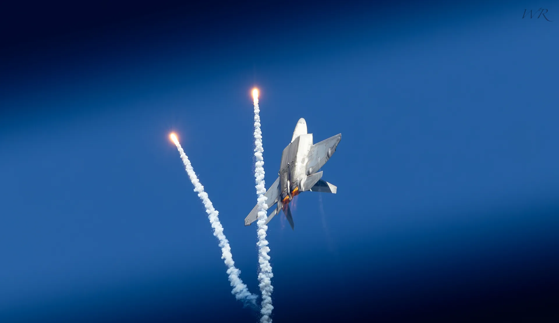 Fighter jet climbing through the sky with smoke trails