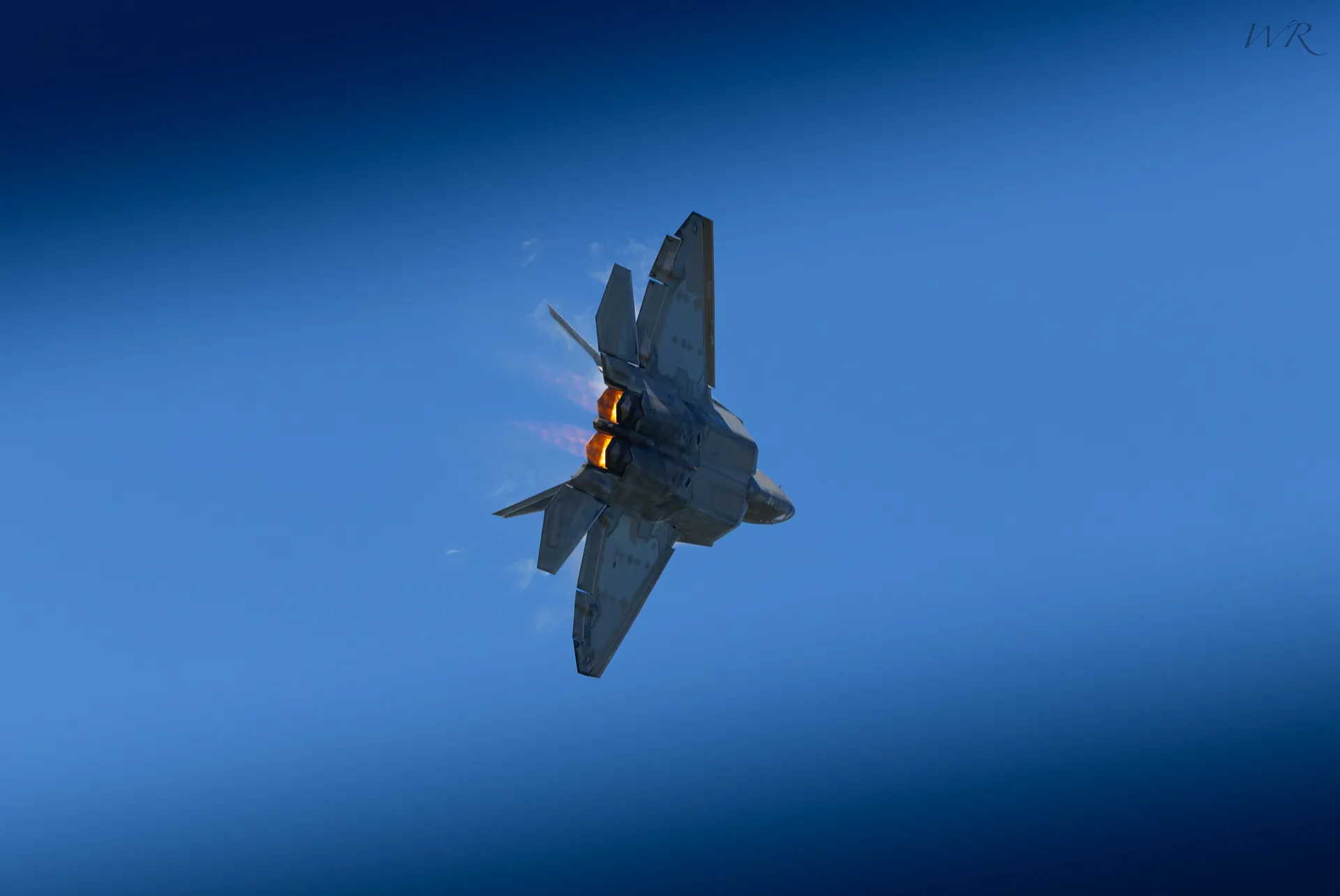 Fighter jet viewed from below with its afterburner glowing